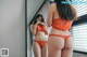 A woman in an orange lingerie standing in front of a mirror.