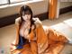 A woman in an orange kimono sitting on the floor.