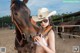 A woman in a cowboy hat holding a rifle next to a horse.